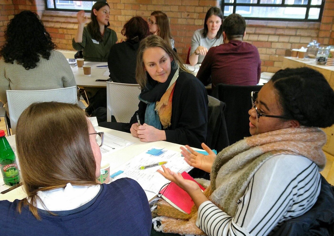 Three people sat at a table with whiteboard paper, sticky notes and pens in front of them. They are deep in discussion.