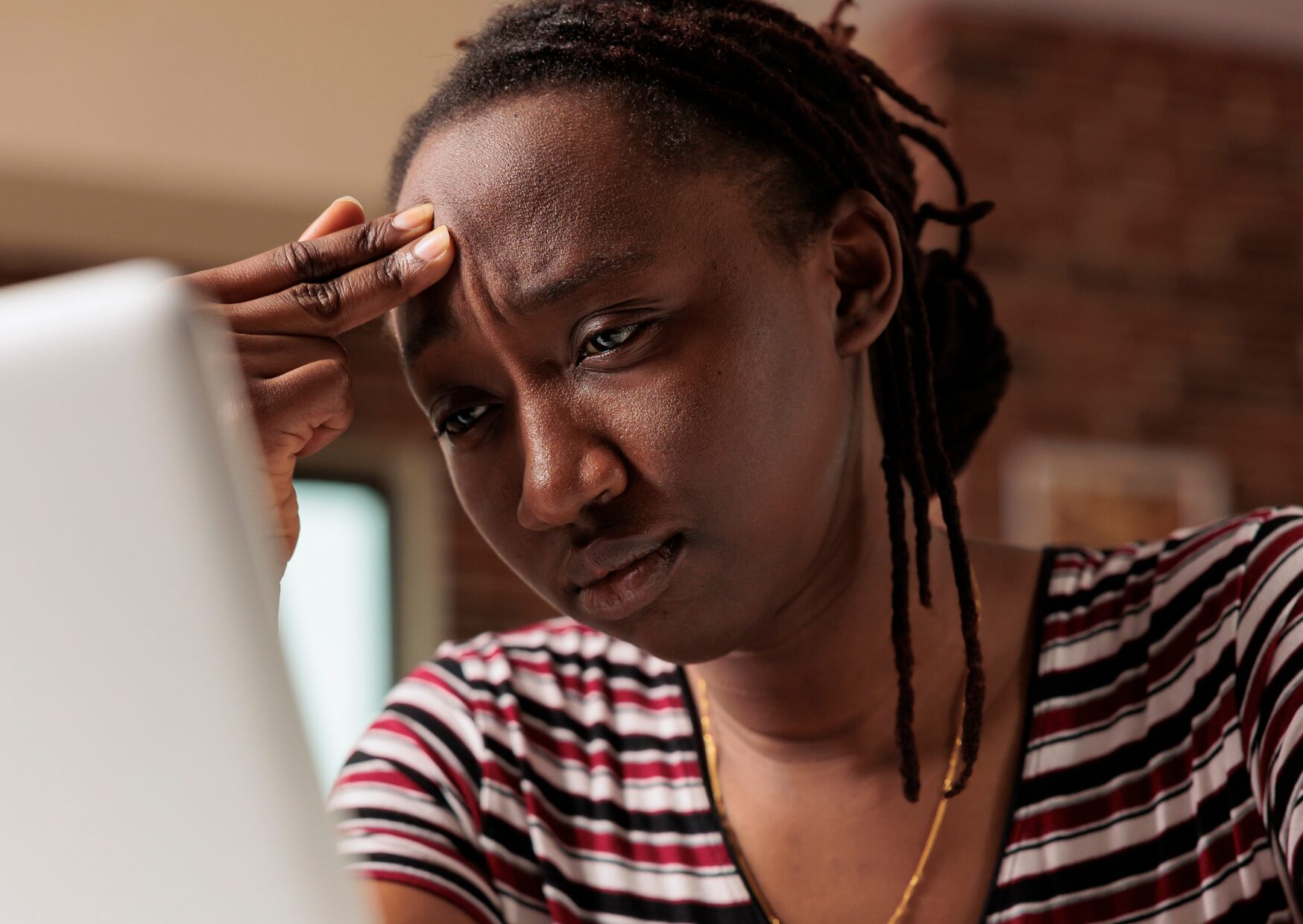 Upset looking person in stripy top. Holding her fingers to her temple whilst looking at a computer screen.