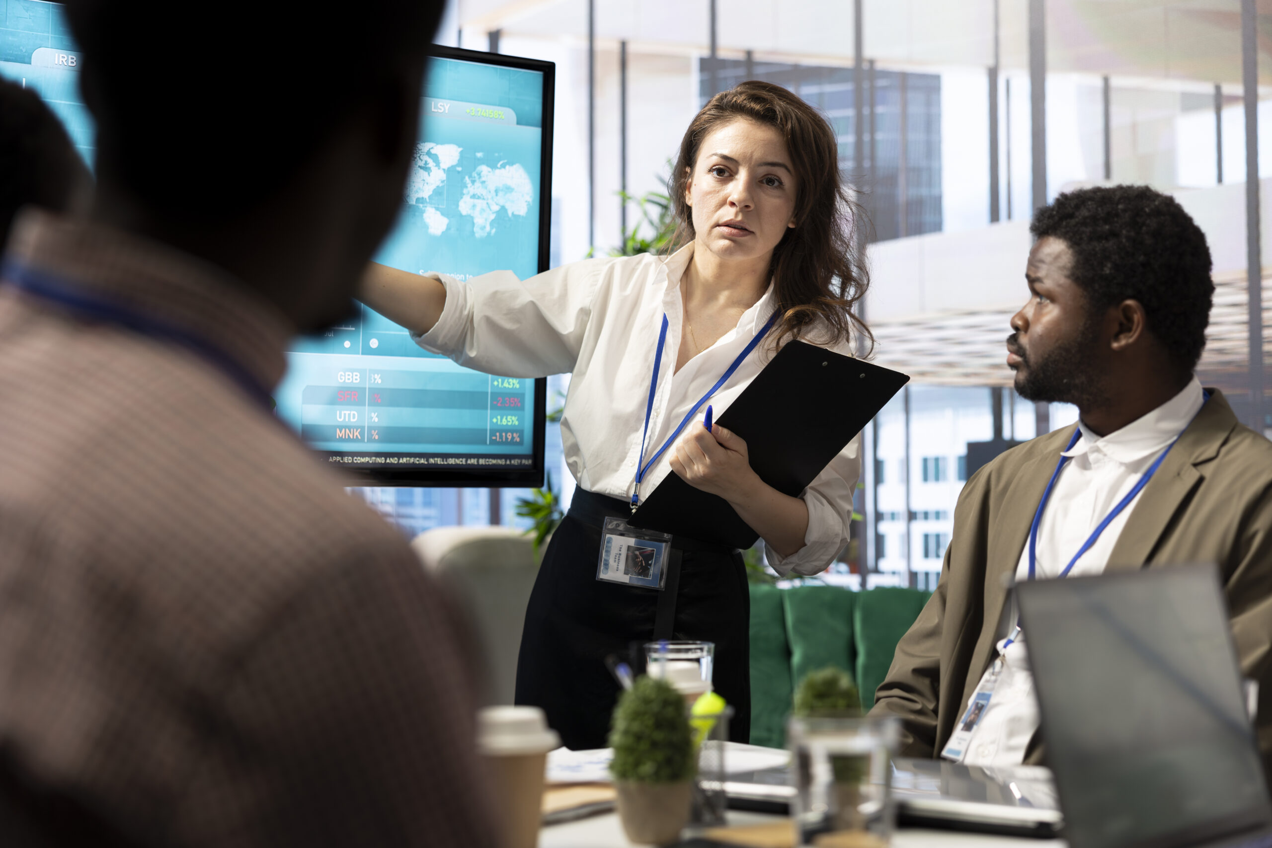 People in office environemnt, female is stood giving a presentation on a screen to two people sat down listening
