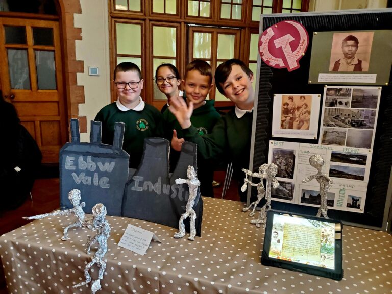 Children standing in front of table with artwork model figures. 
