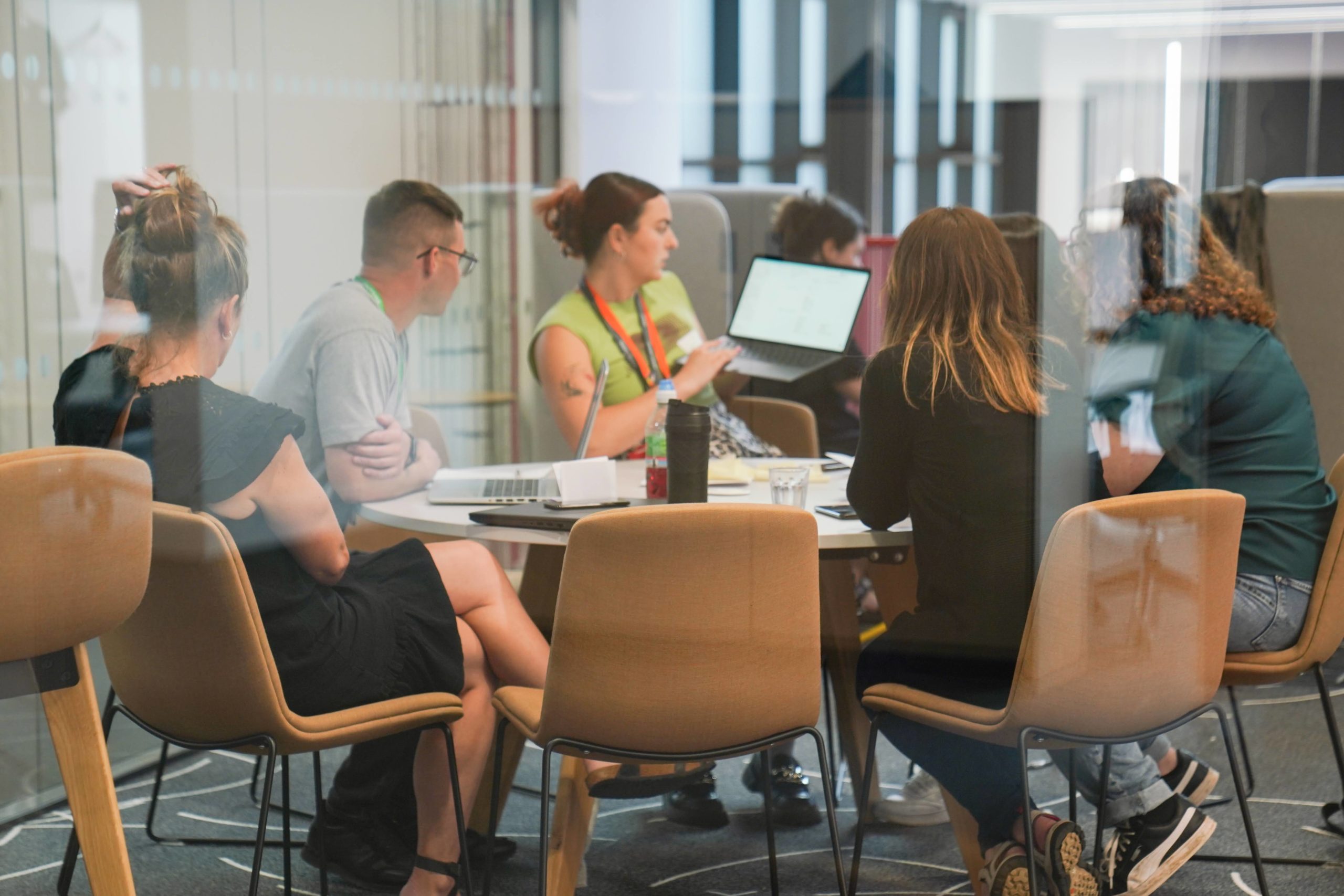 Group of people sat in a small conference room table, looking at a laptop screen being presented.