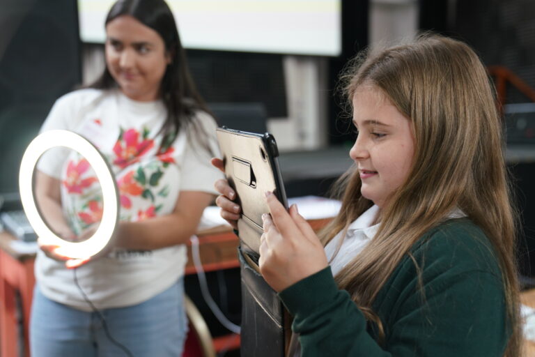 Young girl holding up an iPad and staff member holding a light-up device. 