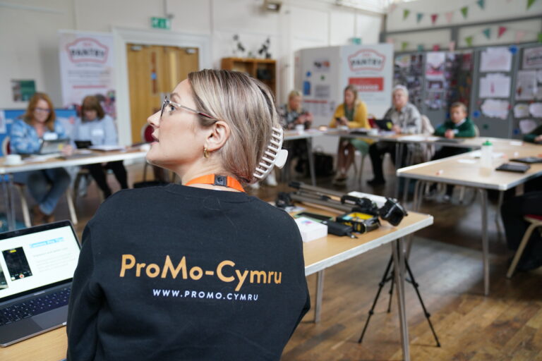 1. A focused woman in a black shirt working on a laptop at a table, presenting to a room of people. 