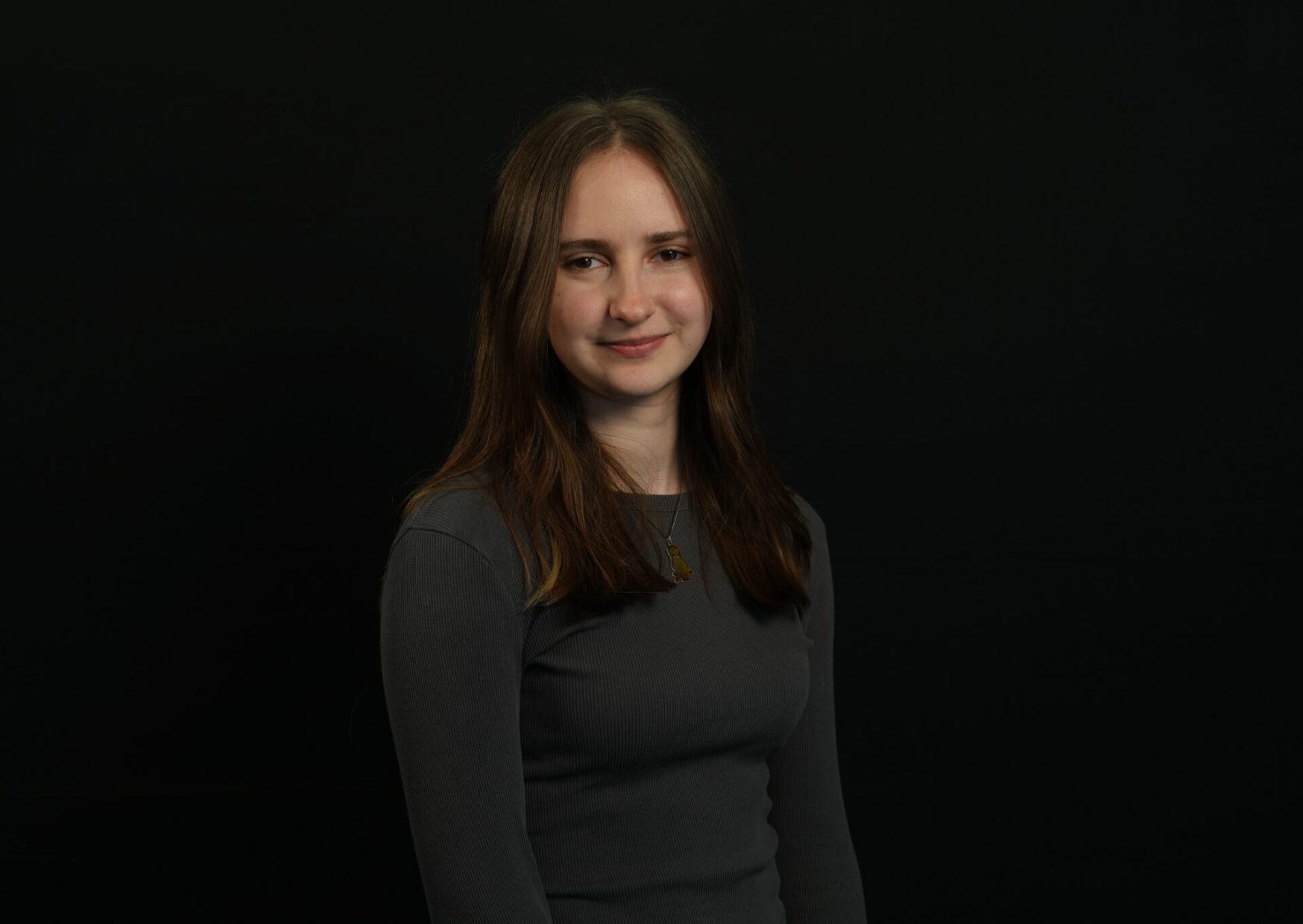 Portrait image of a young, white employee smiling at the camera. She has long brown straight hair.