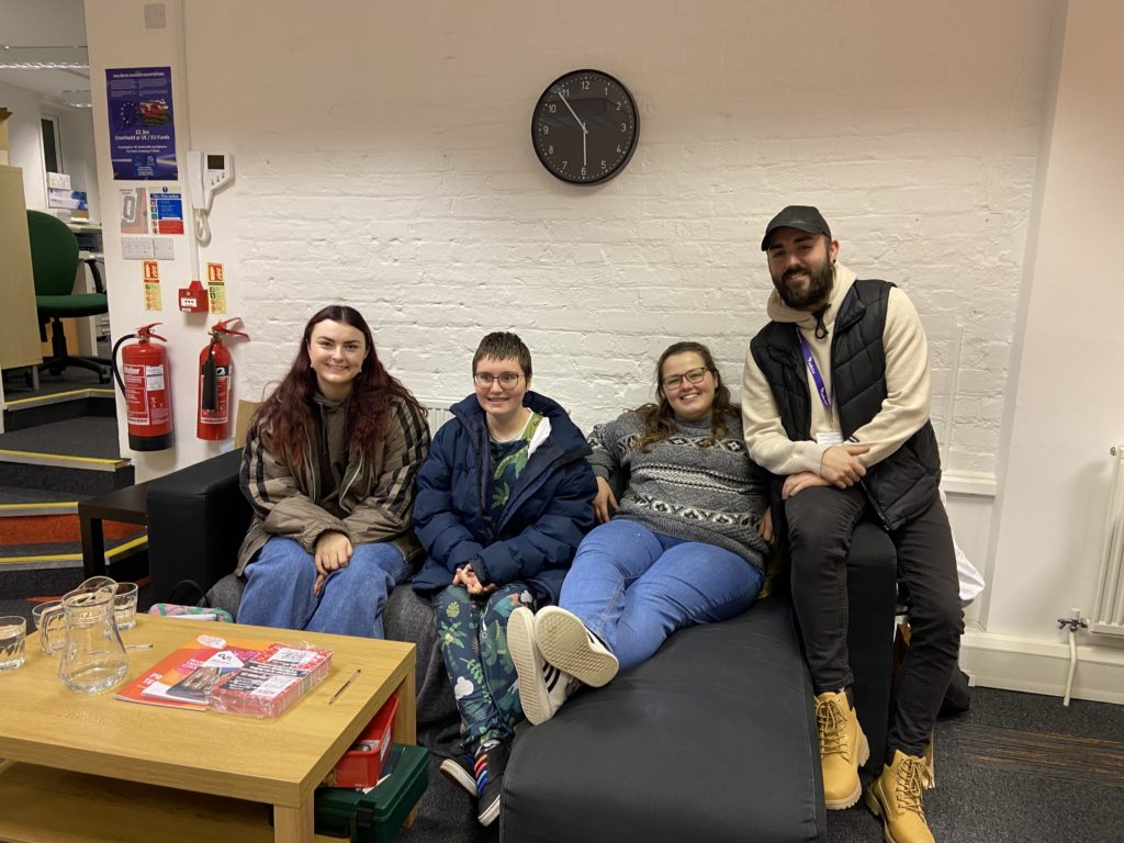 Four people sitting on a couch in front of a clock.