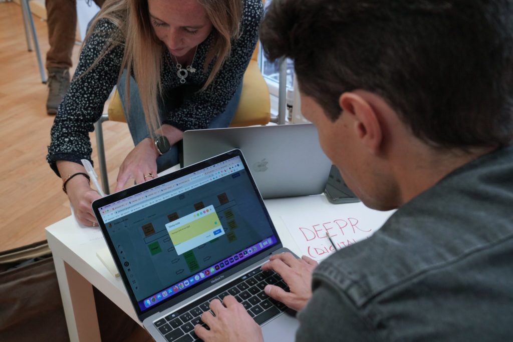 Man working on laptop as woman writes notes on paper on table. 