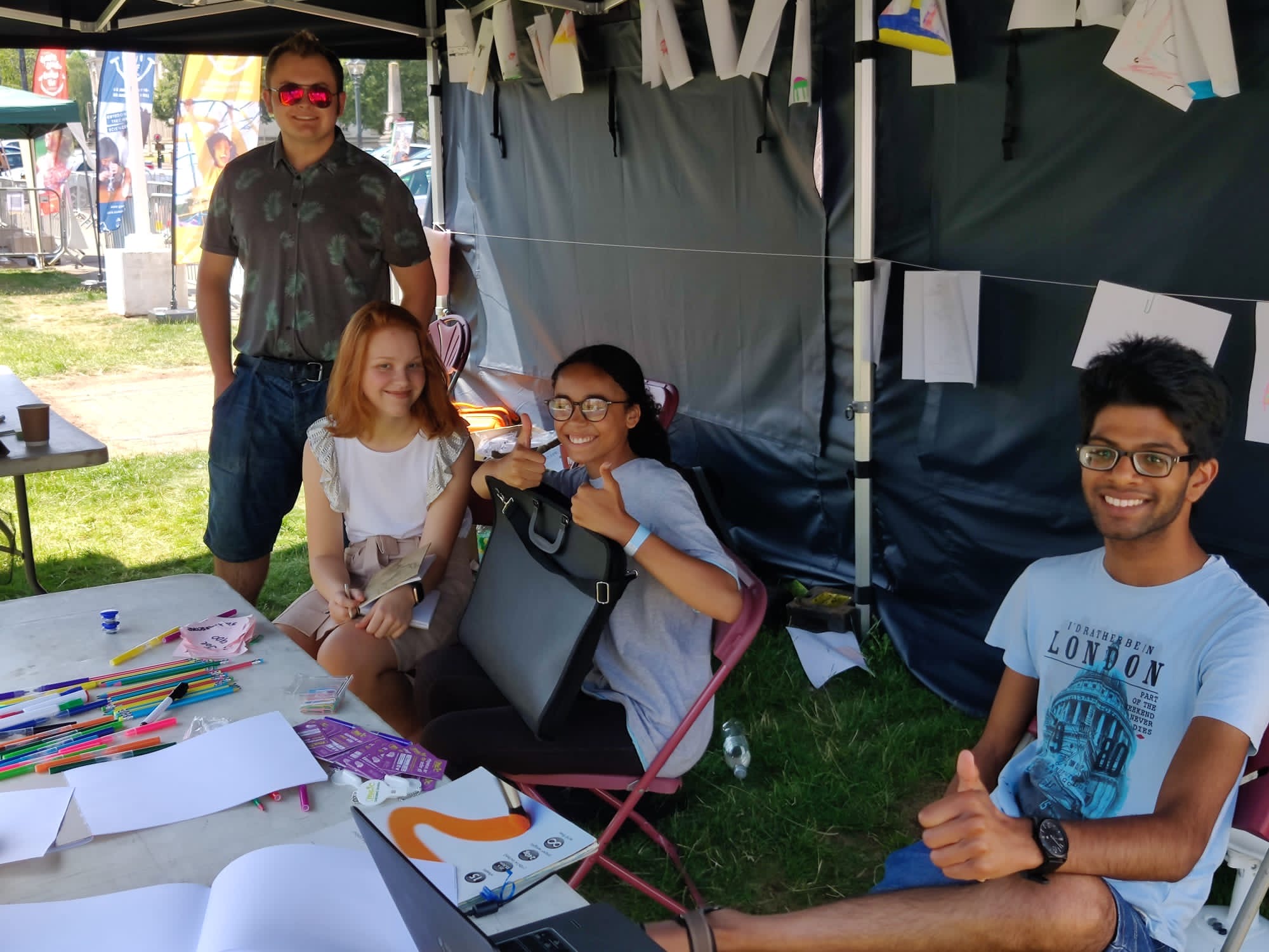 A diverse group of  young people sitting around a table, putting thumbs up and smiling.