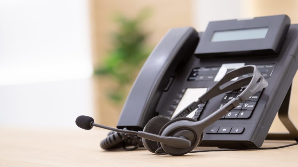 A black traditional office phone with a matching earphones with attached microphone.