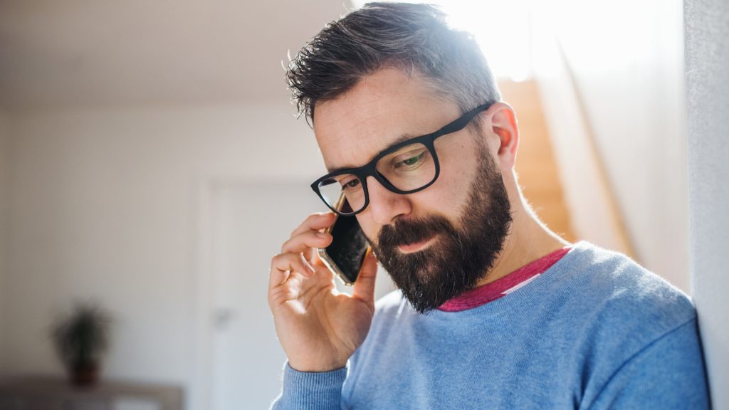 Man listening intently whilst slouched against the wall. He is on a mobile phone call.