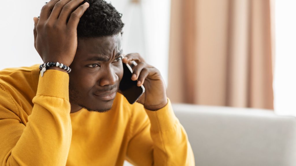 Man sat on sofa on a phone call, with his head in his hands. He looks concerned.