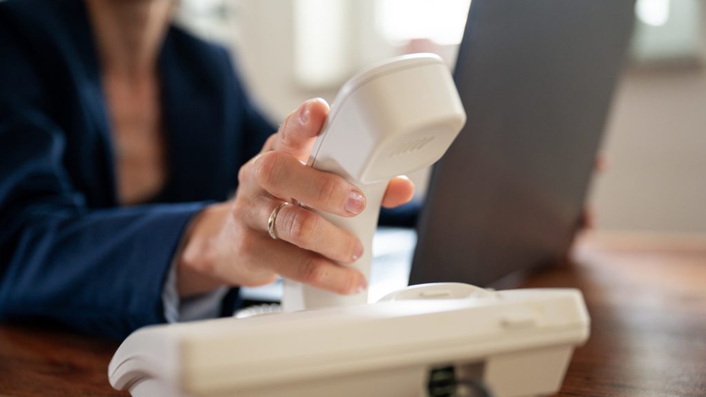 A person putting down the handset onto a traditional office phone dock.