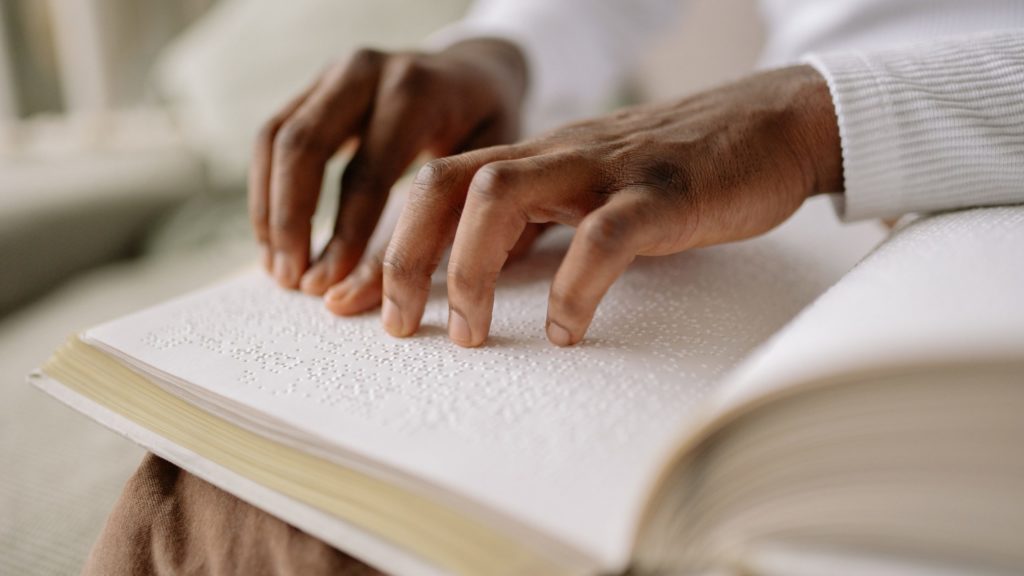 Hands tracing braille in a book.