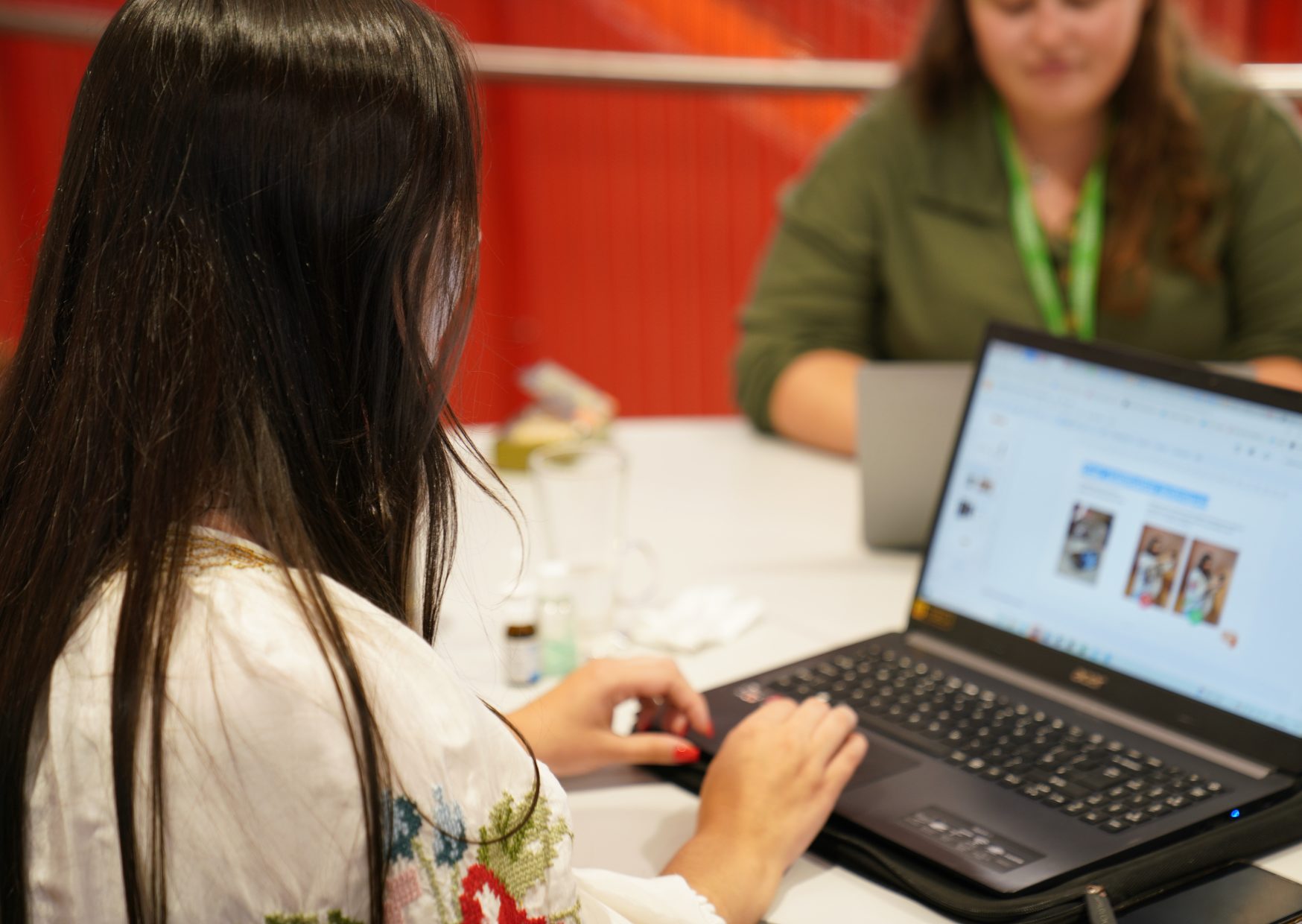 Two people working on a joint table. One persons laptop screen is visible, and they are working on a website.