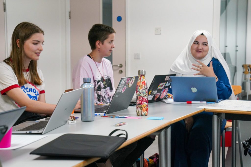 Three young people sat together at tables using laptops