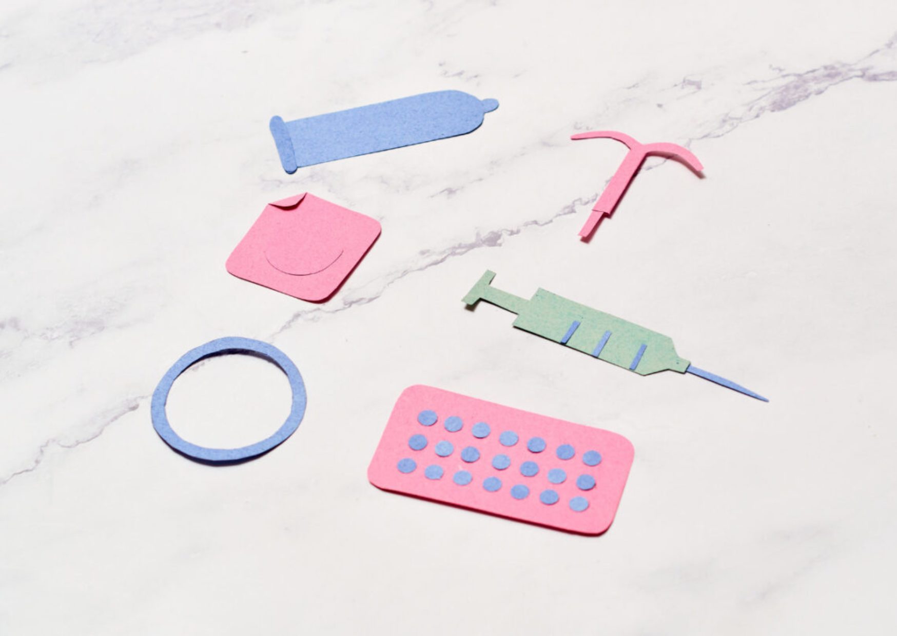 Marble counter top covered in cut out paper images of sexual health icons, such as condoms, the pill and an IUD.