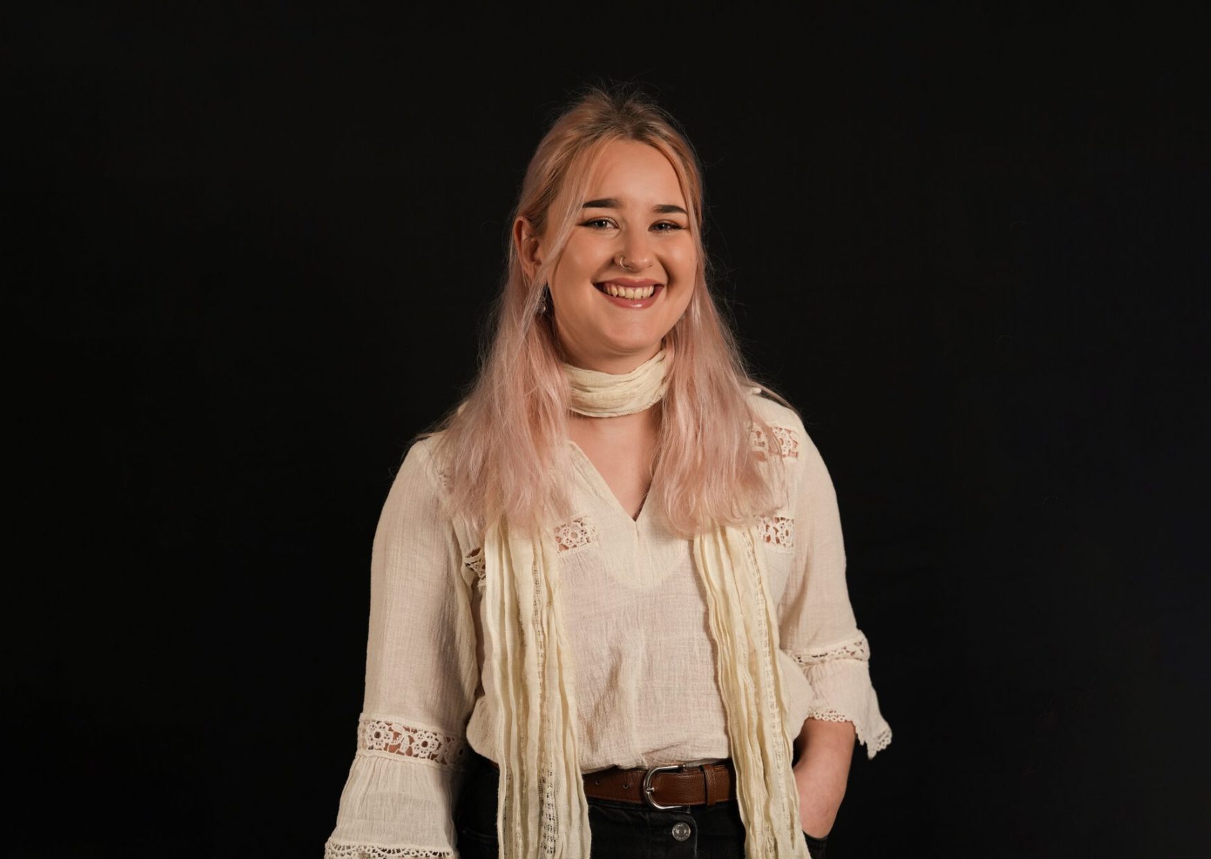 Portrait of Ffion, with light pink hair and white and cream clothing, smiling at the camera