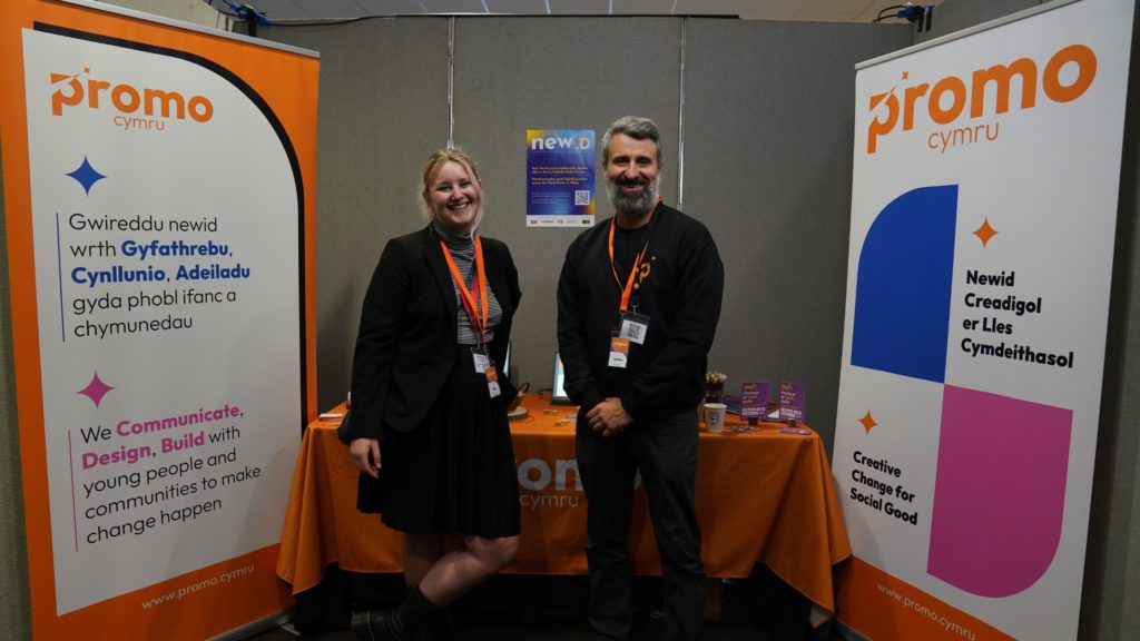 Ffion and her colleague, Nathan, stood in front of a ProMo Cymru stall with branded banners and a tablecloth. 