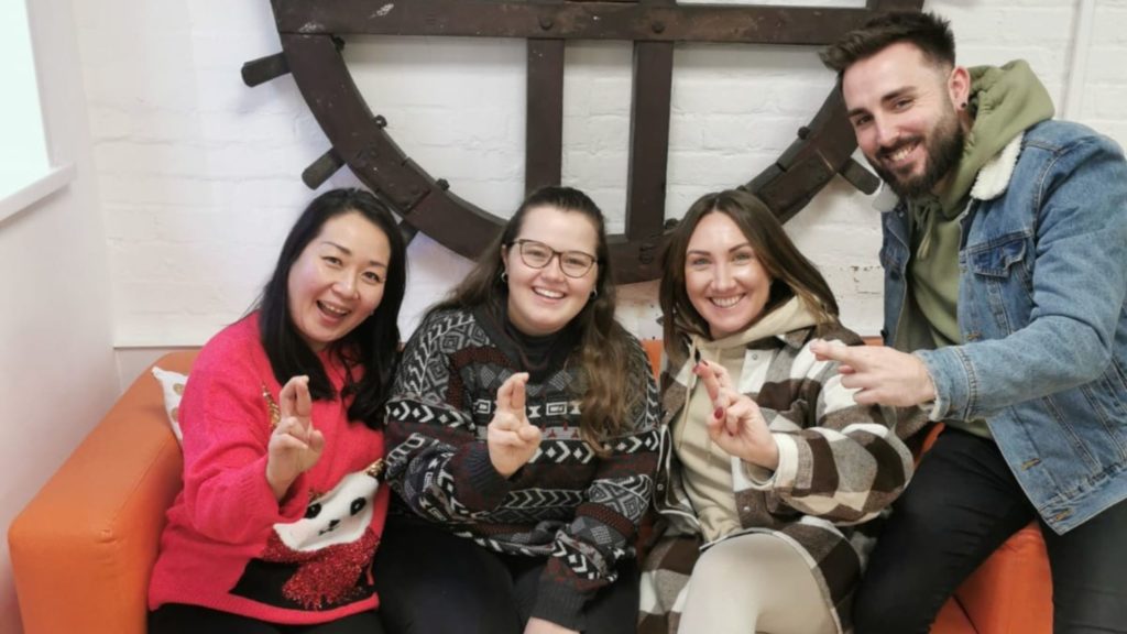 Four staff members sat on an orange sofa, crossing fingers.