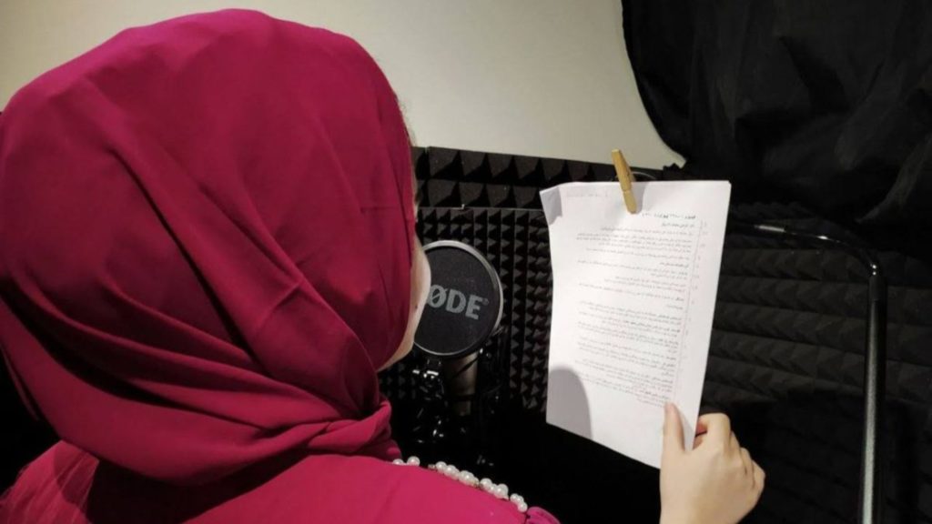 Girl wearing hijab speaks into a Rode microphone whilst reading off a script