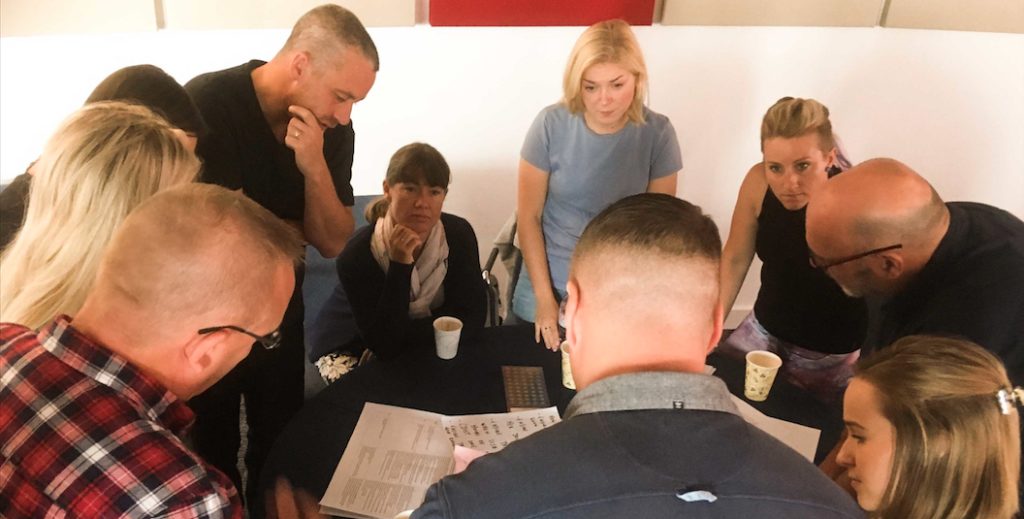 A group of 10 people huddled around a desk in discussion