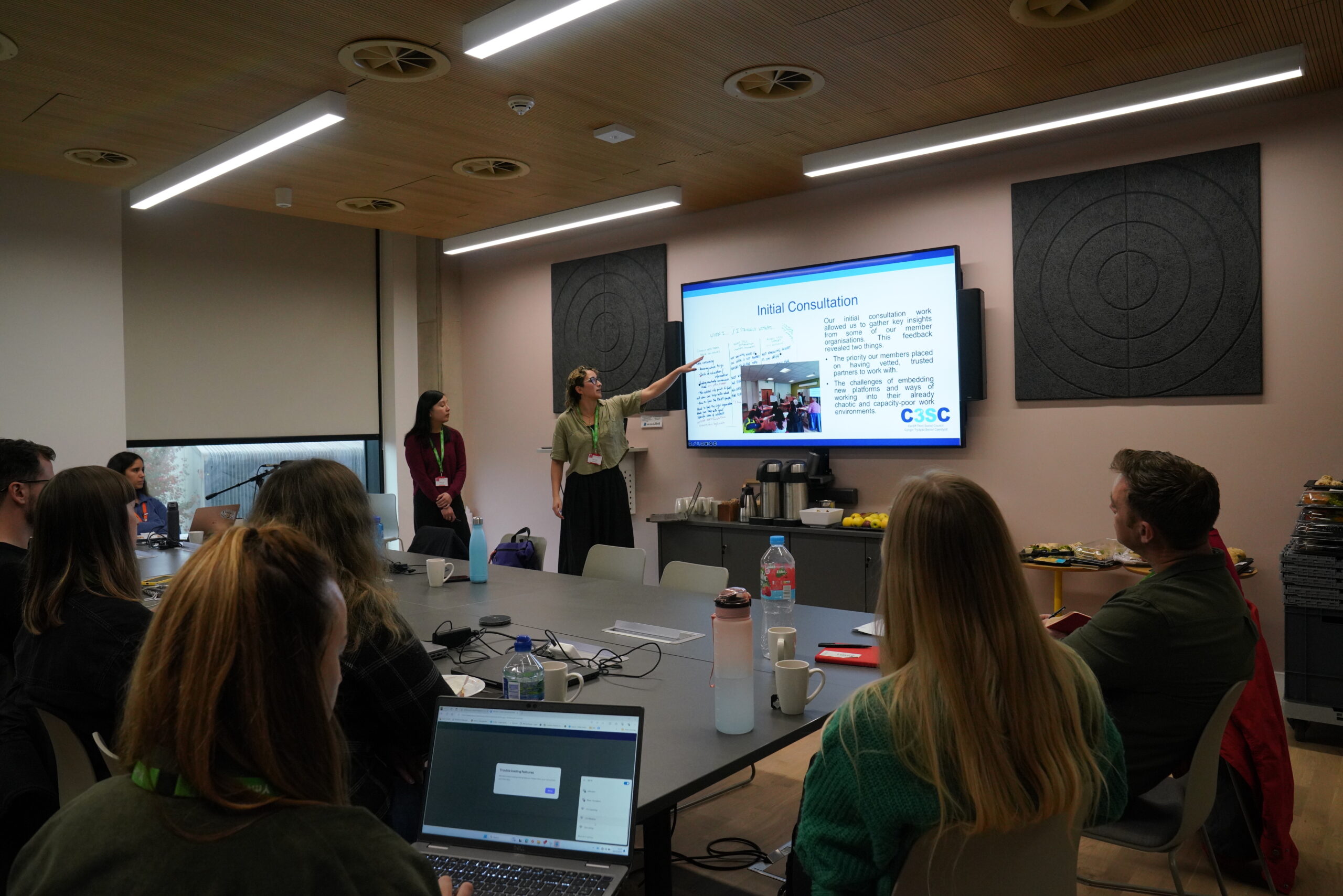 Group of professionals from different organisation sat around a table whilst two staff members from C3SC are giving a presentation