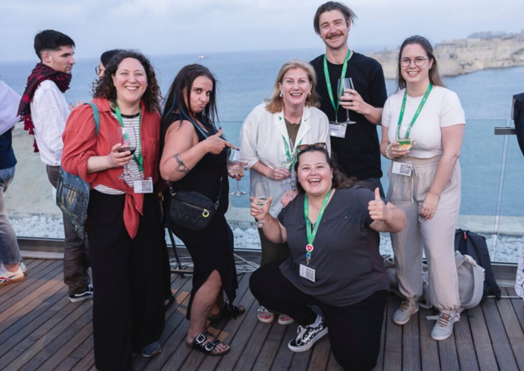 A group of people smiling and holding drinks on a rooftop terrace overlooking the sea.