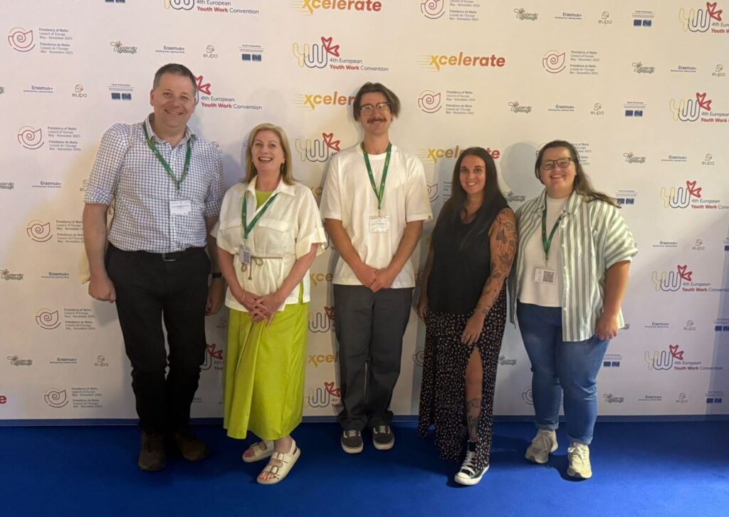 A group of five professionals, including Halyna (far right), pose in casual but smart attire at the 4th European Youth Work Convention, with the official event branding visible behind them.
