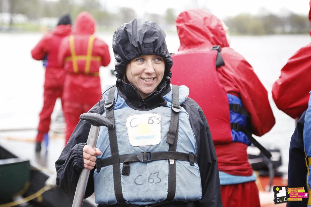 A young woman (Arielle) in wet weather gear with a paddle in her hand smiling.