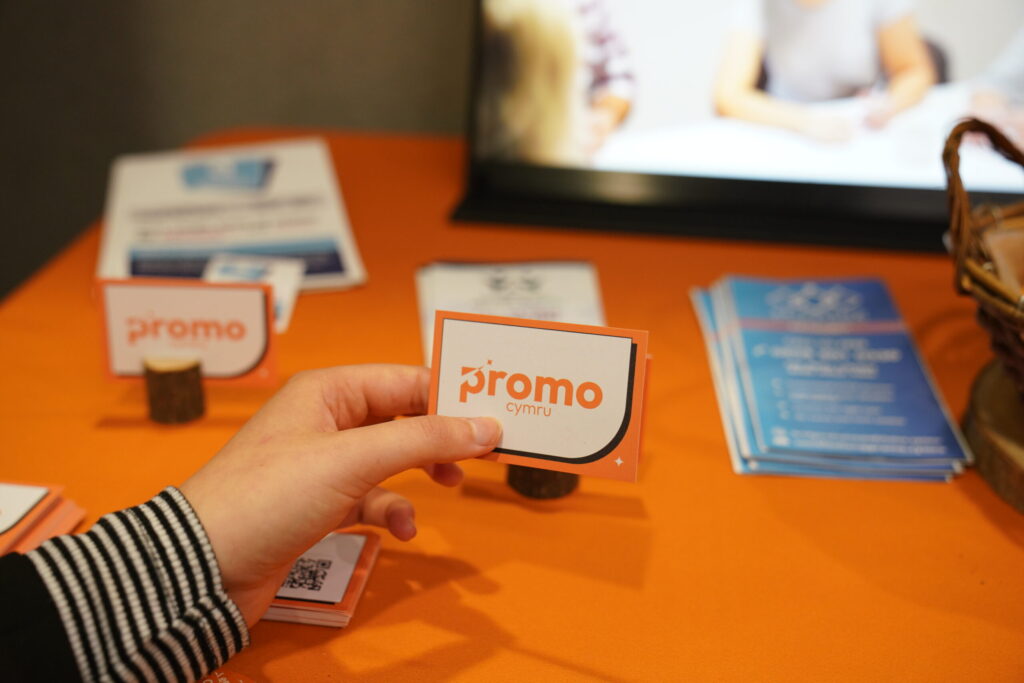 a hand holding a business card with the words promo cymru on it - showing the new branding developed