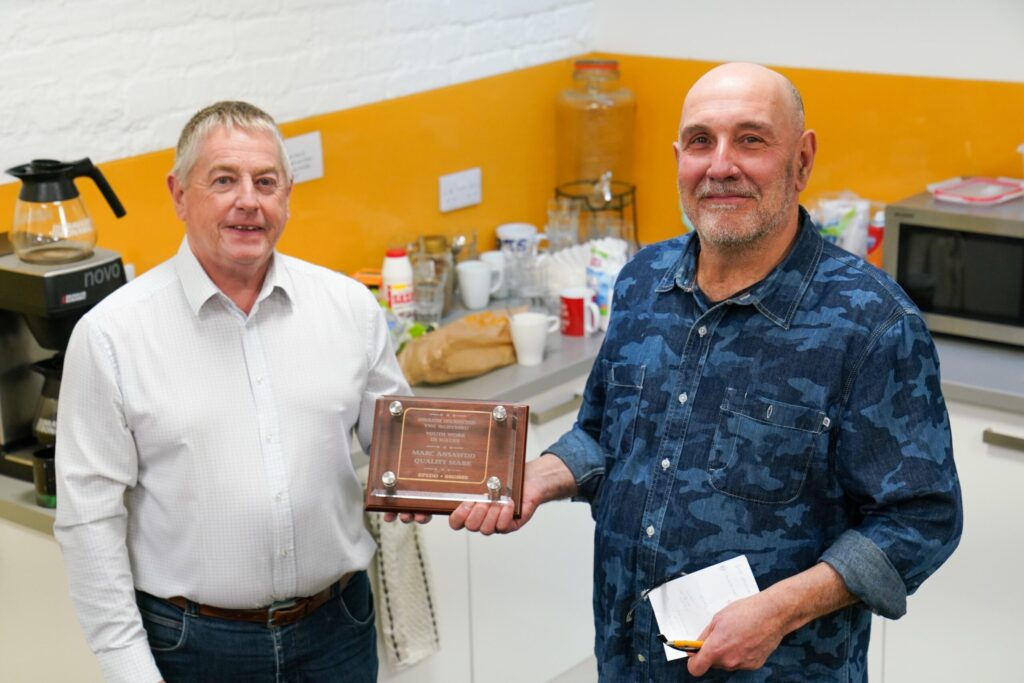 Two men holding a award between them smiling at the camera.