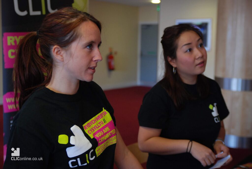 Two young women (Arielle and CIndy) wearing black tshirts with neon writing saying 'CLIC You are connected) staring at someone off camera