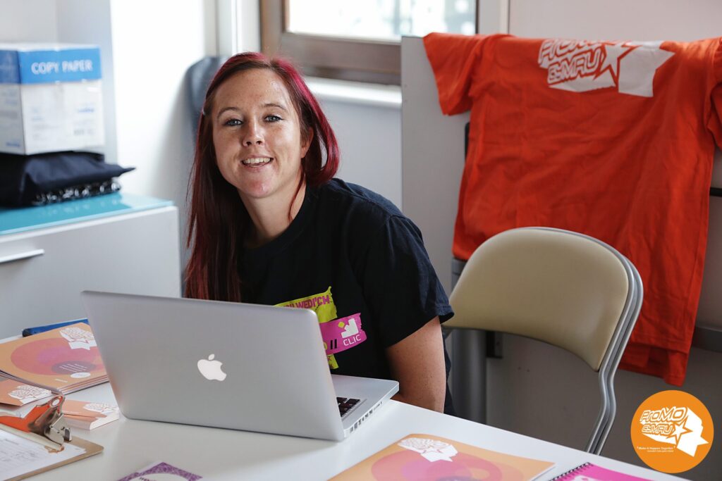 A young woman (Arielle) sat at a desk with a laptop in front of her smiling at the camera