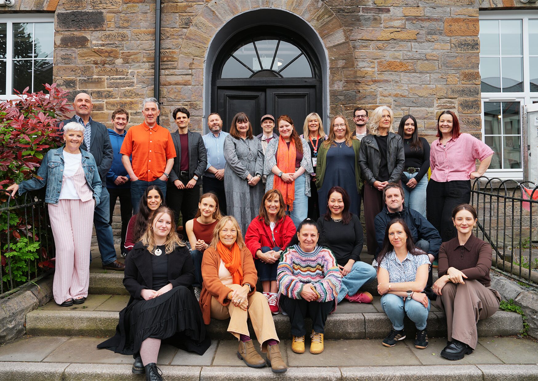 Staff photo of people sat and standing on steps outside a building
