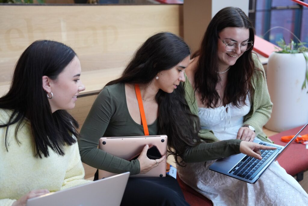 Three females sat chatting and looking at a laptop together smiling.