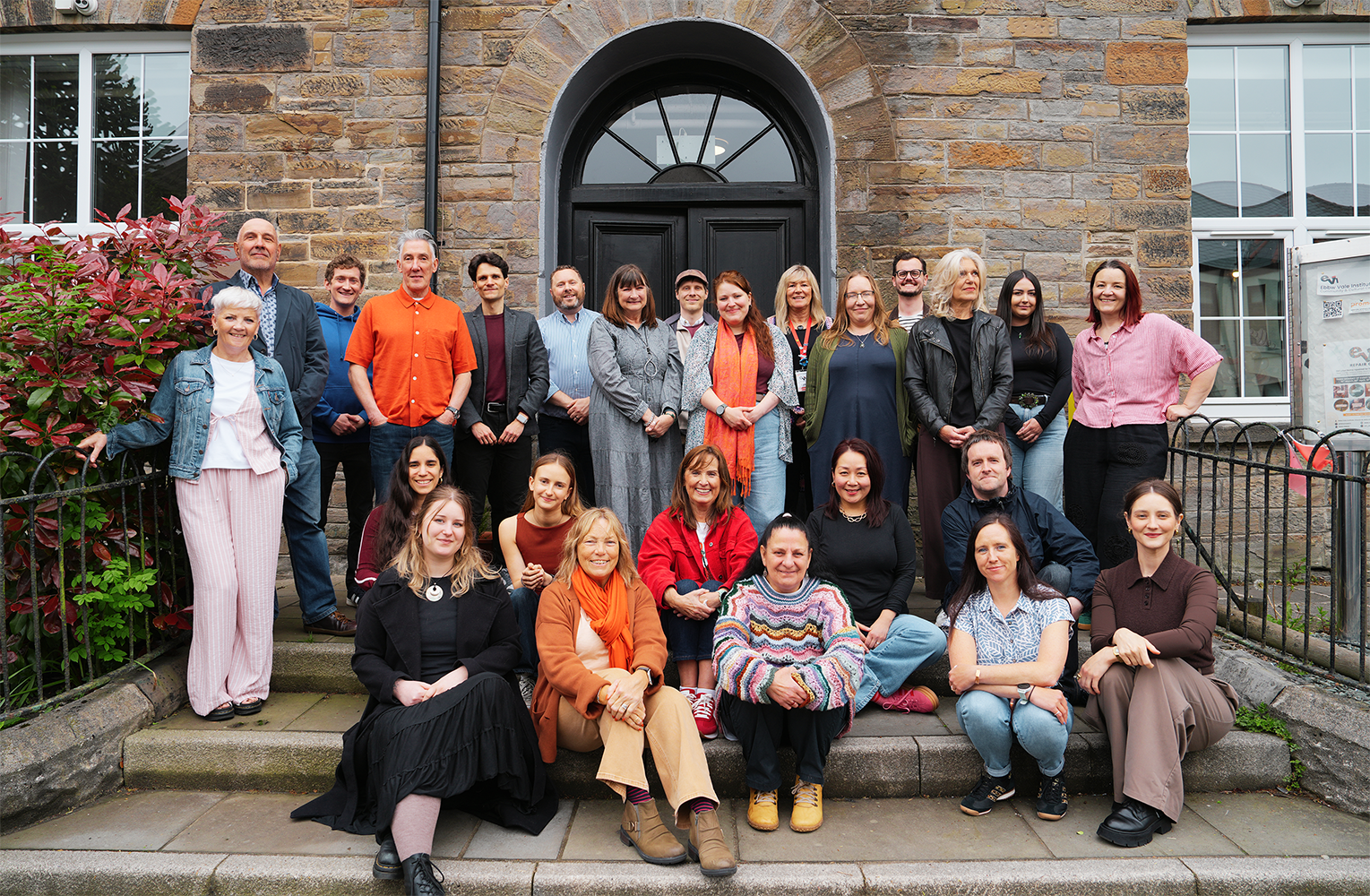 Staff photo of people sat and standing on steps outside a building