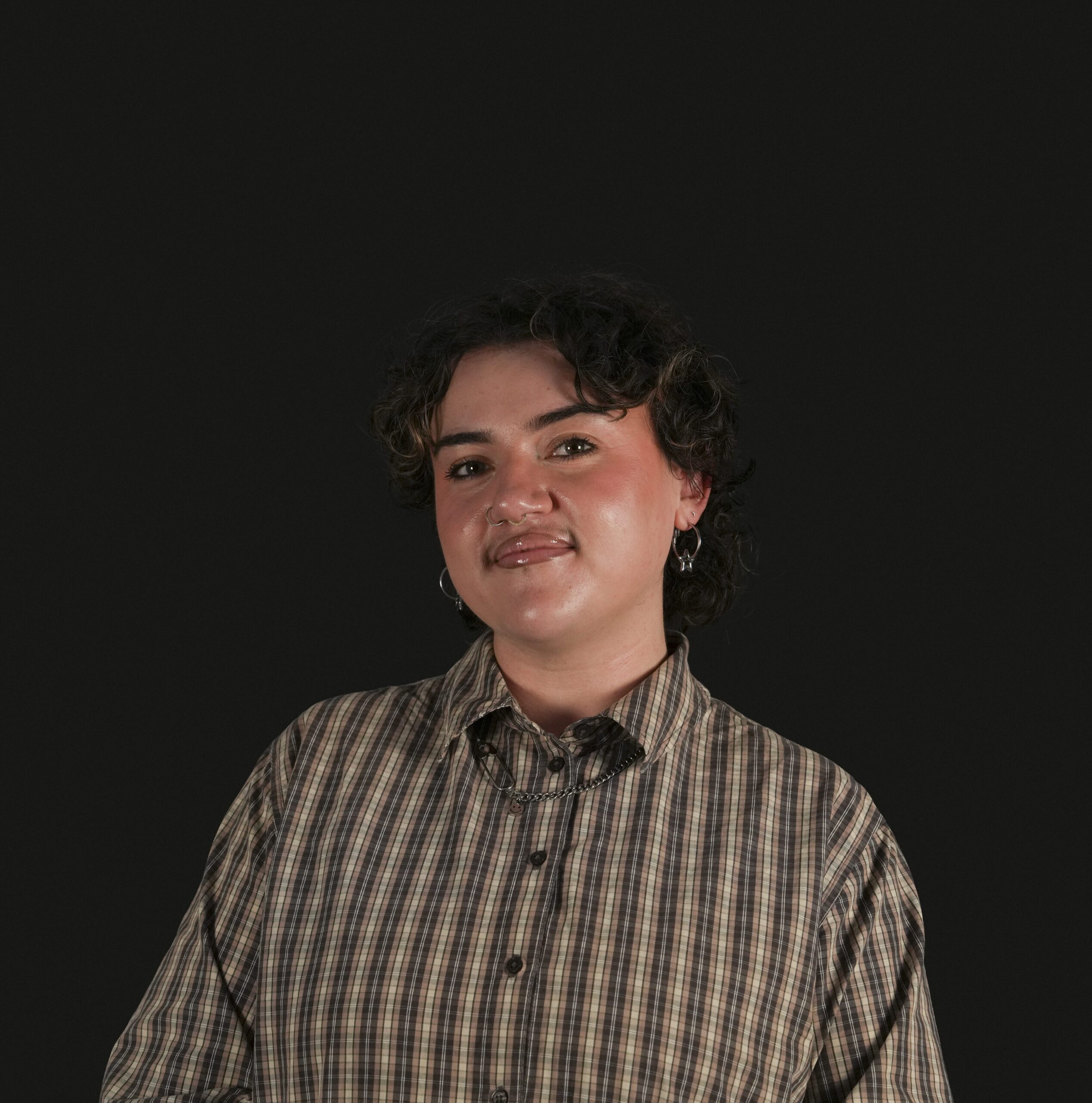 Bethan against a black background wearing a brown plaid shirt, smiling.