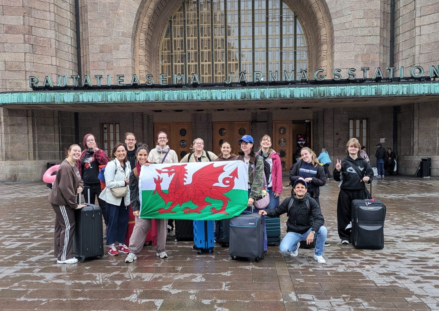 Group photo of MoFG Peer Service Designers with the Welsh Flag outside Helsinki Railway station