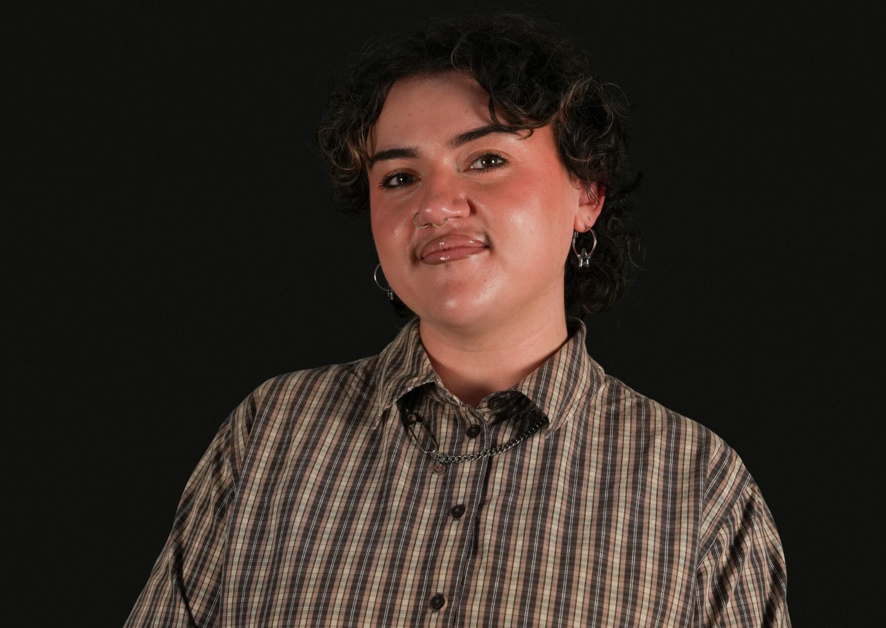 Bethan against a black background wearing a brown plaid shirt, smiling.