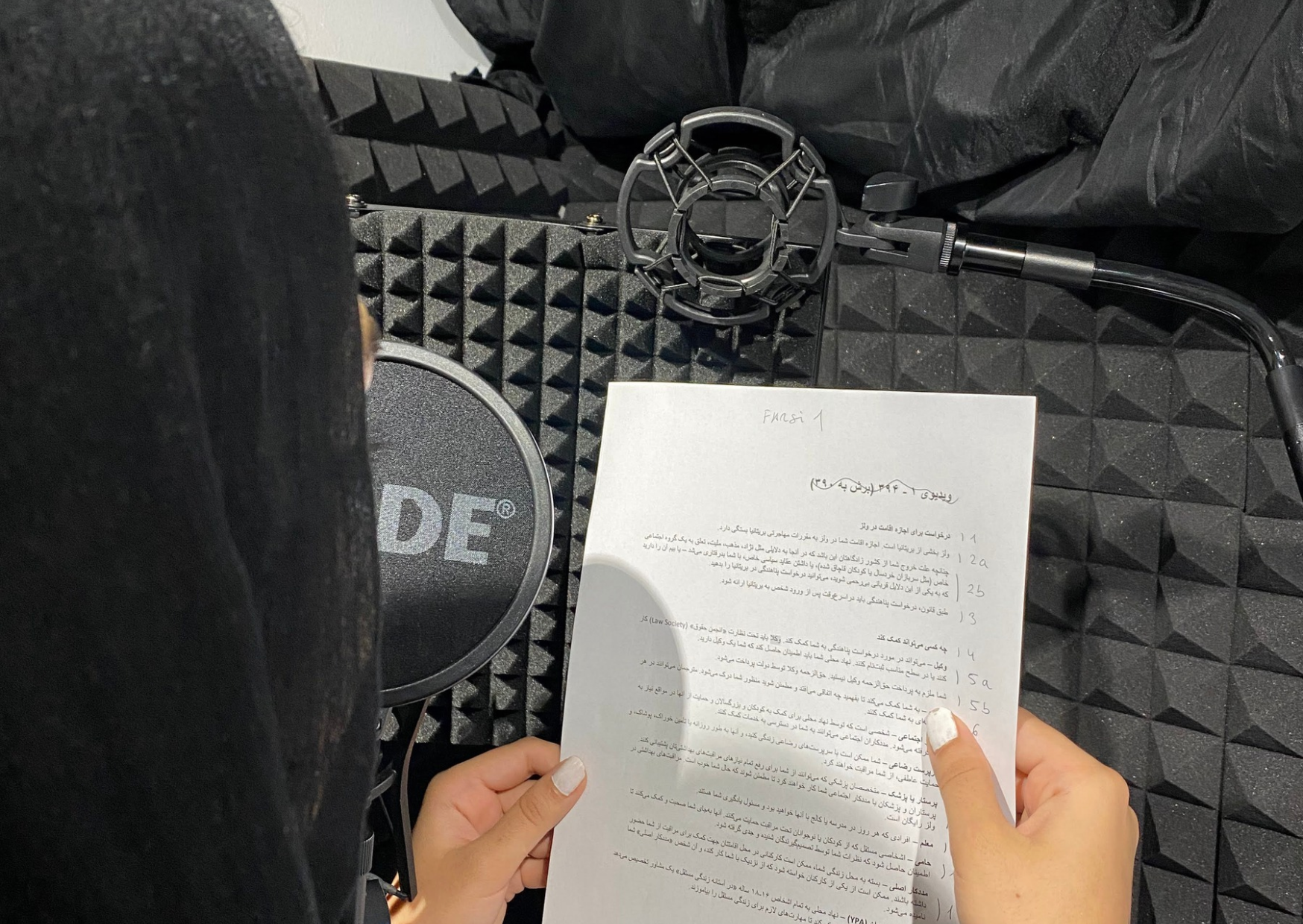 A person in a hijab holding up a script recording a voice over into a rhode mic
