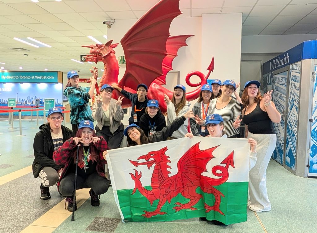Mind Our Future Gwent young people taking a photo with the Welsh flag inside Cardiff airport
